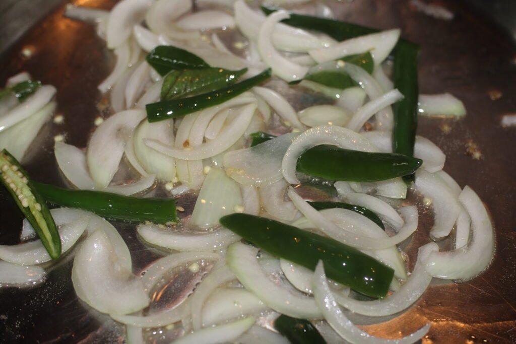 Add the sliced onions, curry leaves, and green chillies.