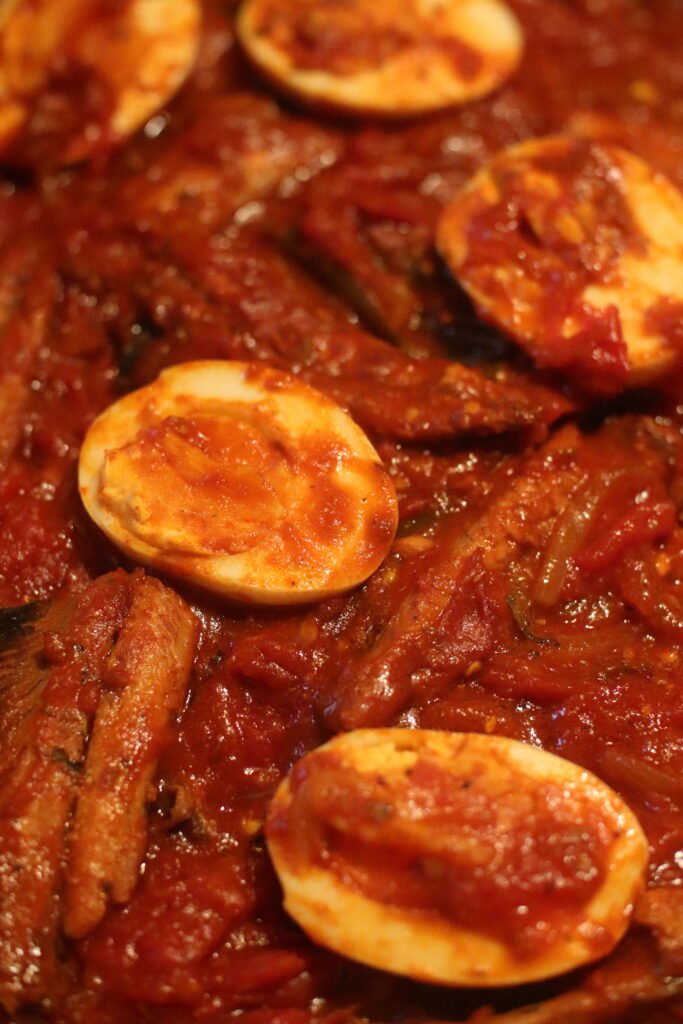 Arrange sliced boiled eggs around the pilchards and lightly spread chutney over them.