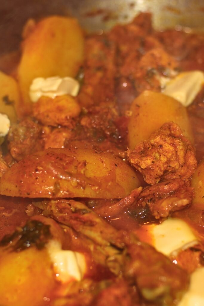 Small pieces of margarine melting into a rich, bubbling Durban chicken biryani masala base on the stovetop