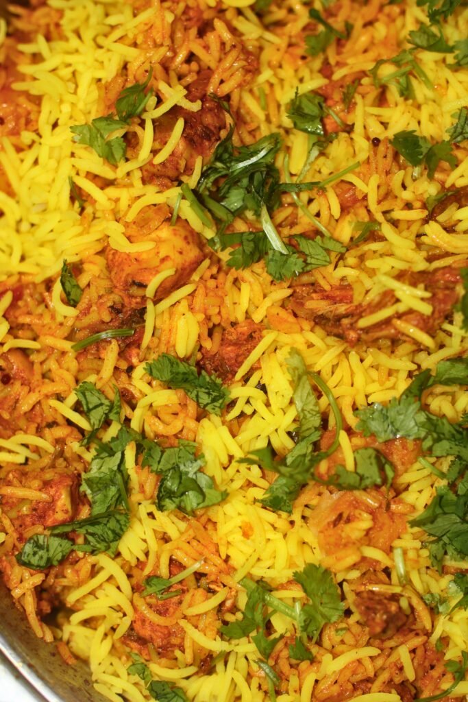 Layering golden parboiled basmati rice over chicken masala and potatoes in a large pot, garnished with fresh chopped dhania.