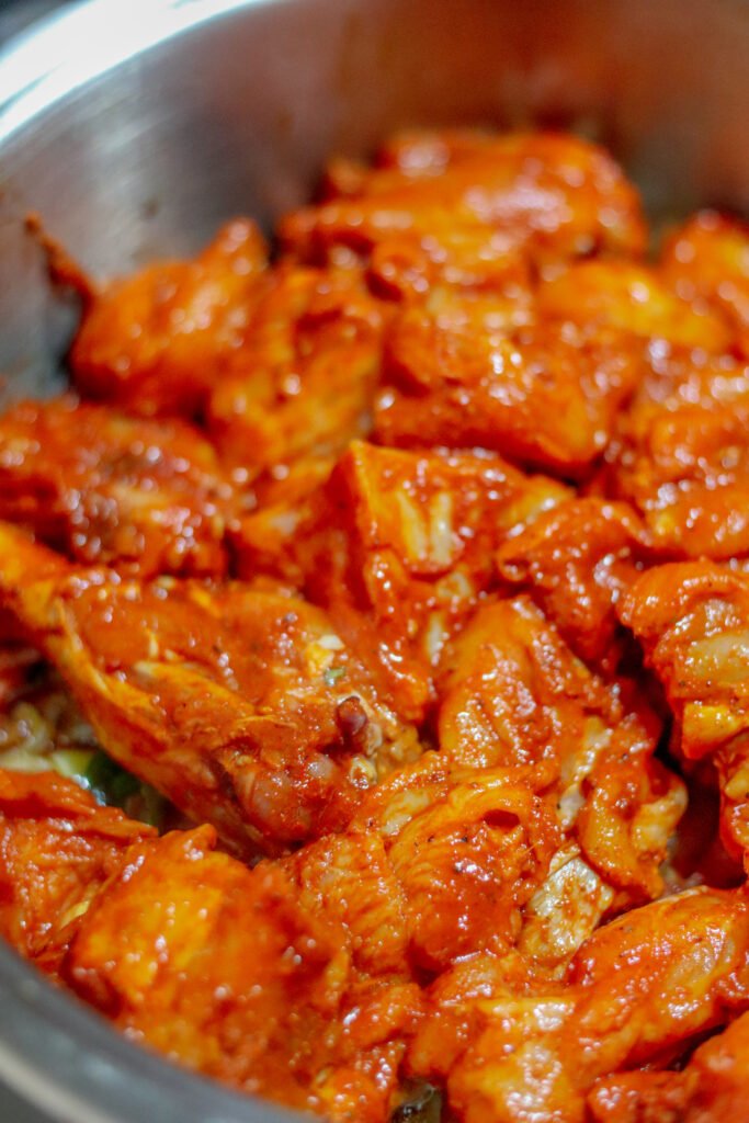 Marinated chicken pieces added to spiced onion and tomato base in pot