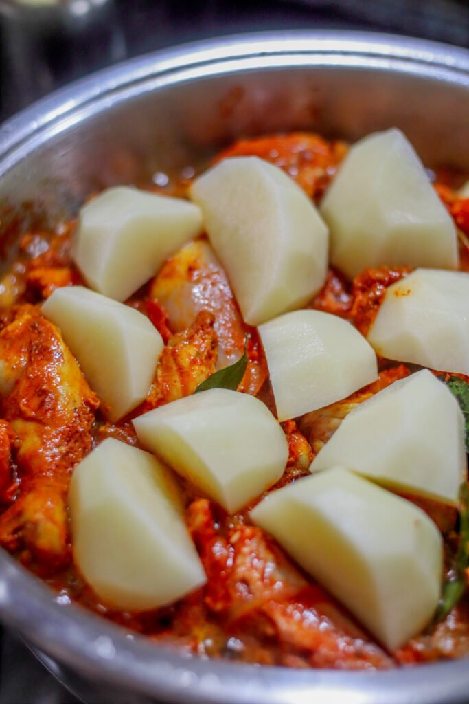Quartered potatoes placed on top of Durban chicken curry in pot