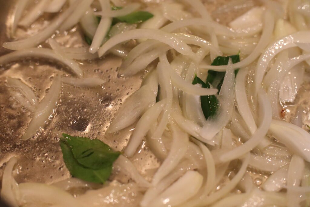 Sliced onions and curry leaves cooking in sunflower oil in a heavy bottomed pot