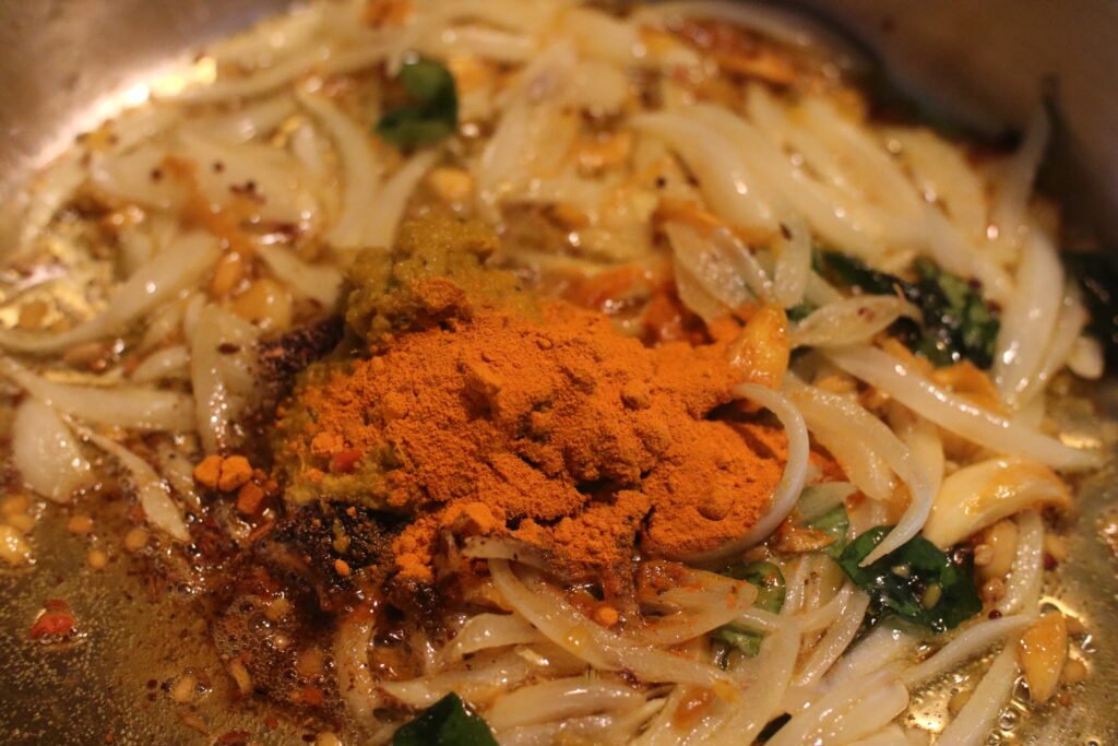 Kashmiri chilli powder turmeric and garam masala added to onions in pot for Durban mutton curry