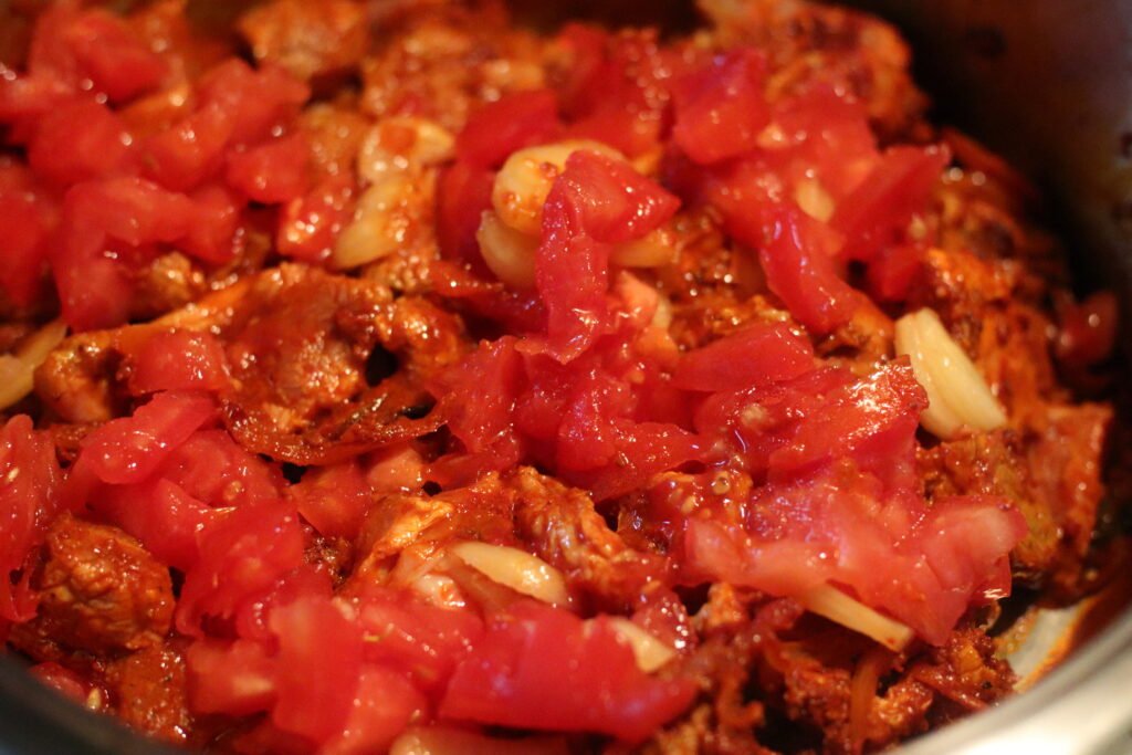 Mutton pieces and chopped tomato added to spice mixture in pot