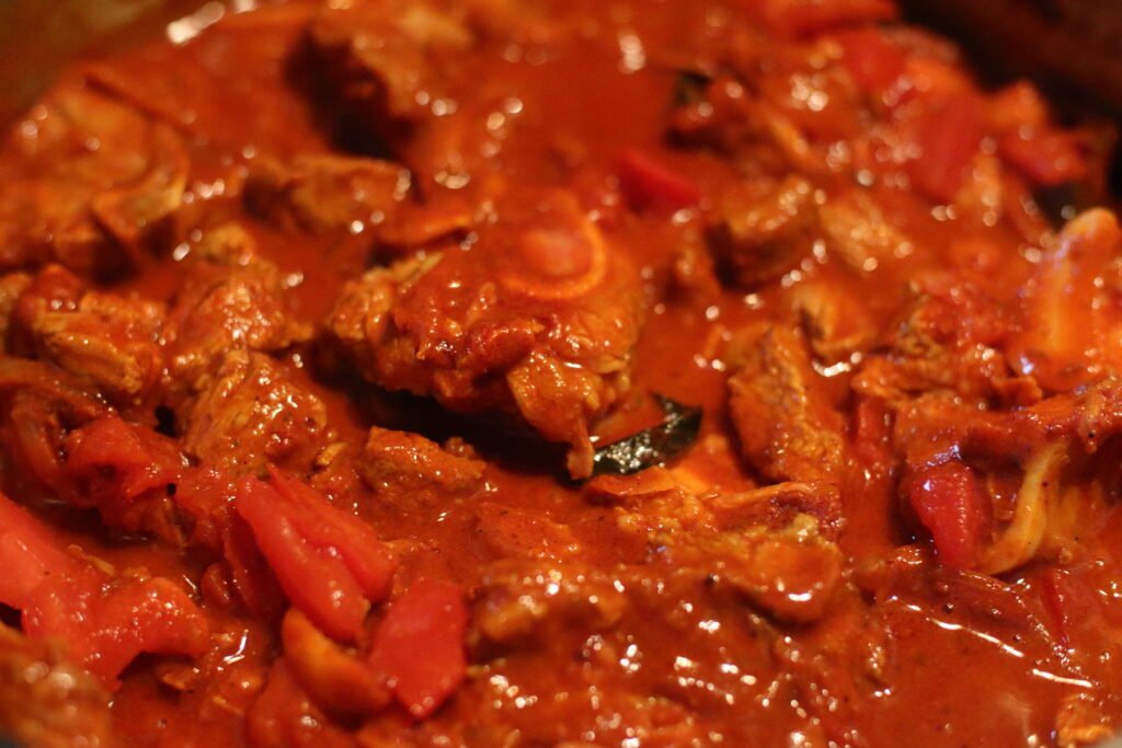 Mutton pieces and chopped tomato mixed with spices in pot