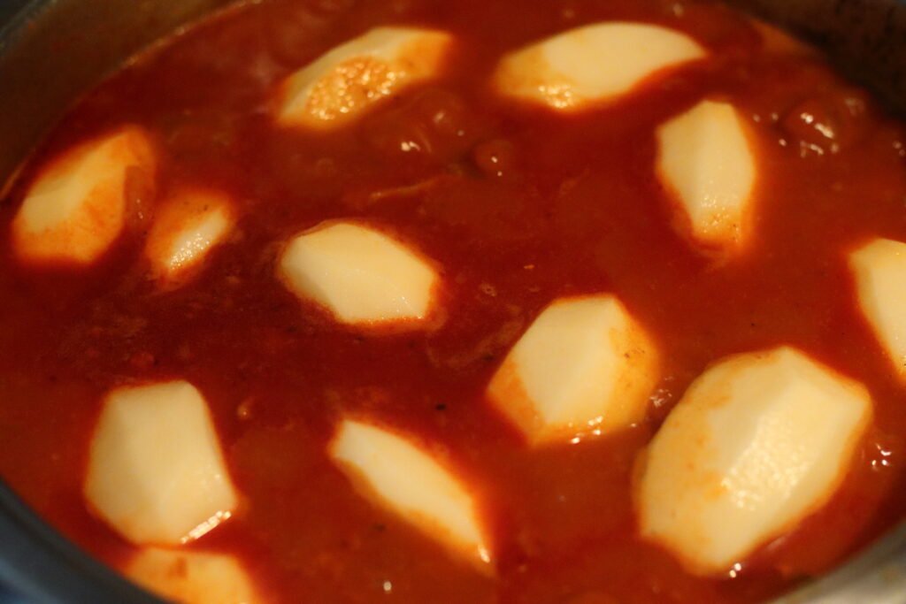 Sliced potatoes added to Durban mutton curry in pot