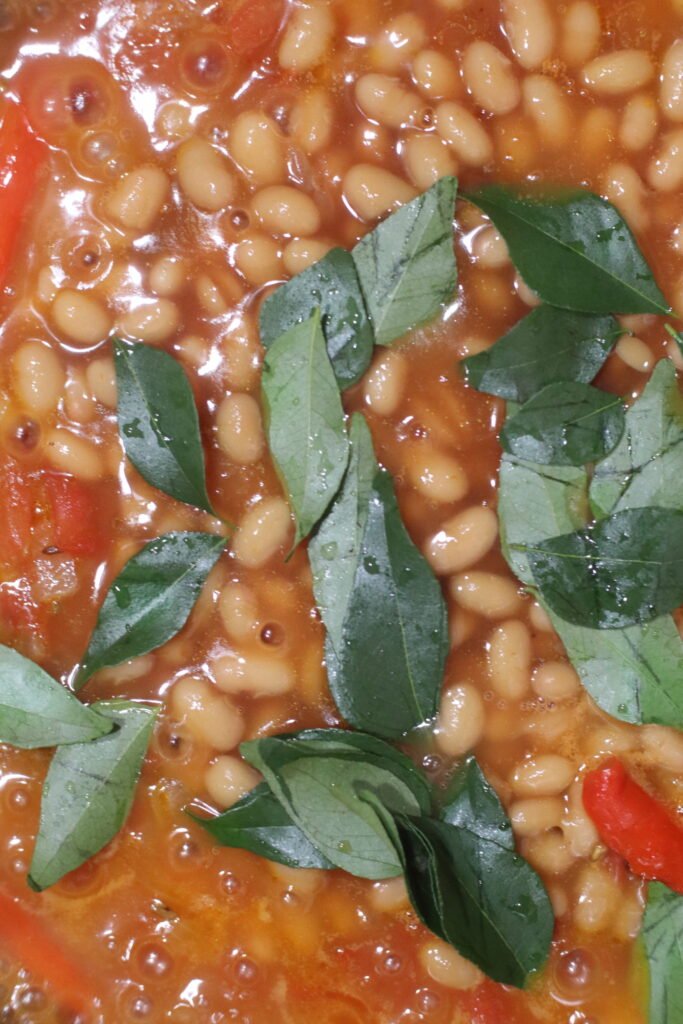Adding baked beans and curry leaves to the spicy tomato mixture