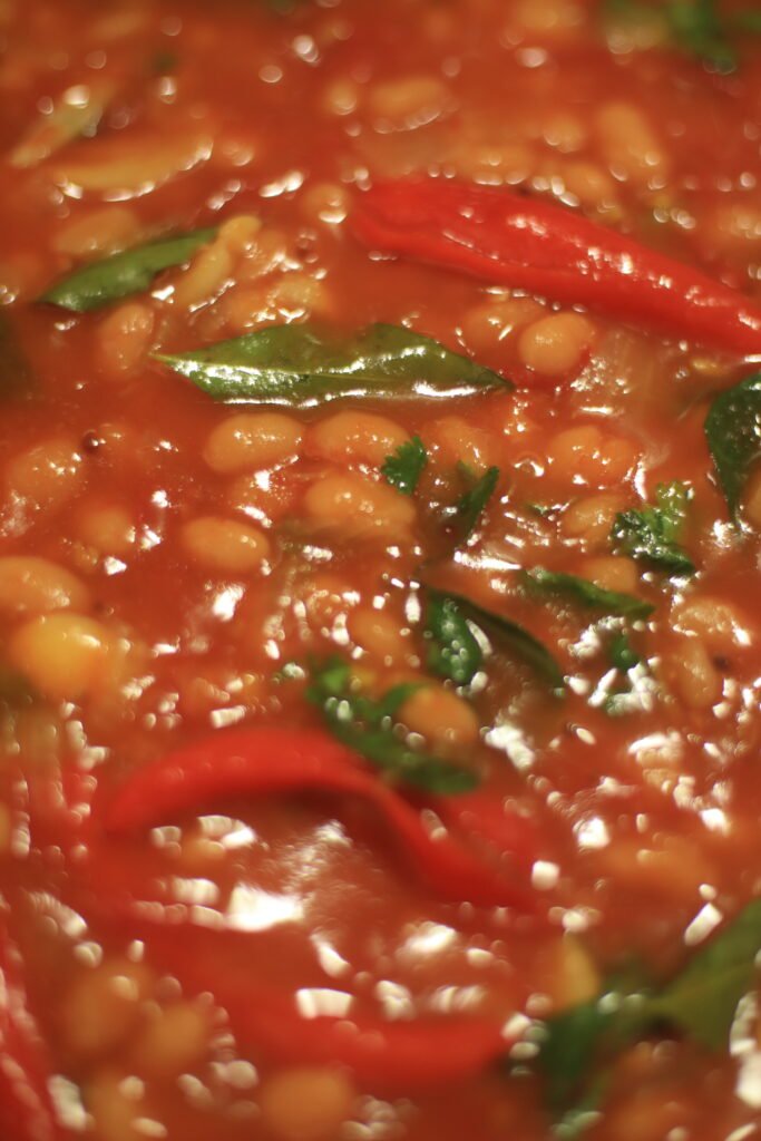 Spicy baked beans simmering in a pot with curry leaves