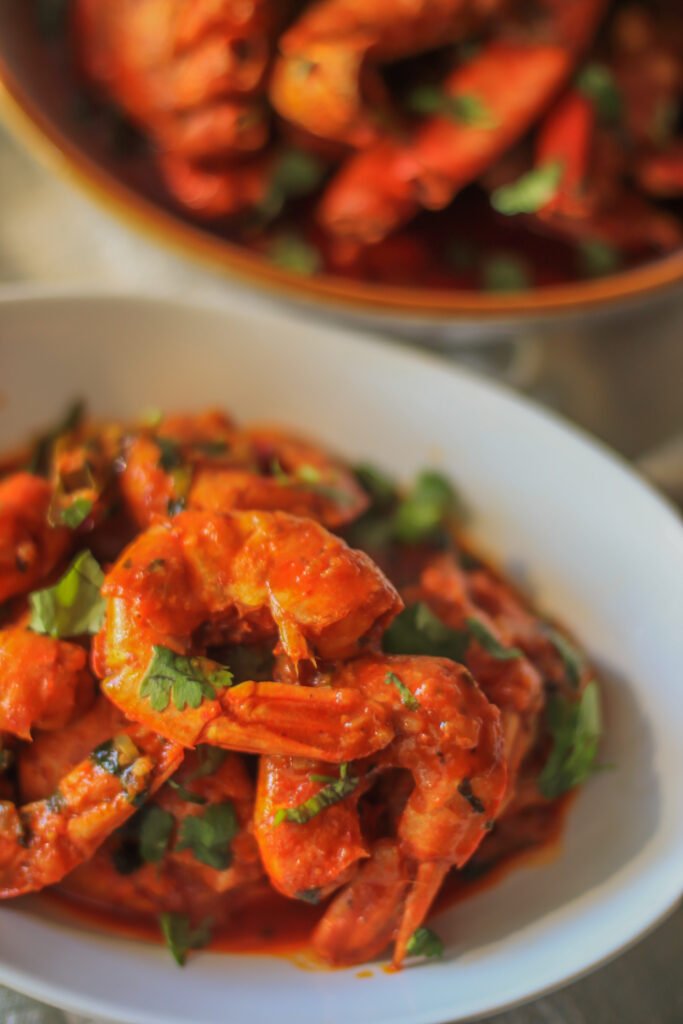 durban chilli garlic butter prawns in bowl with curry leaves and coriander