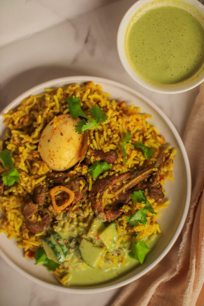 green mutton biryani served on a plate next to sour milk salad