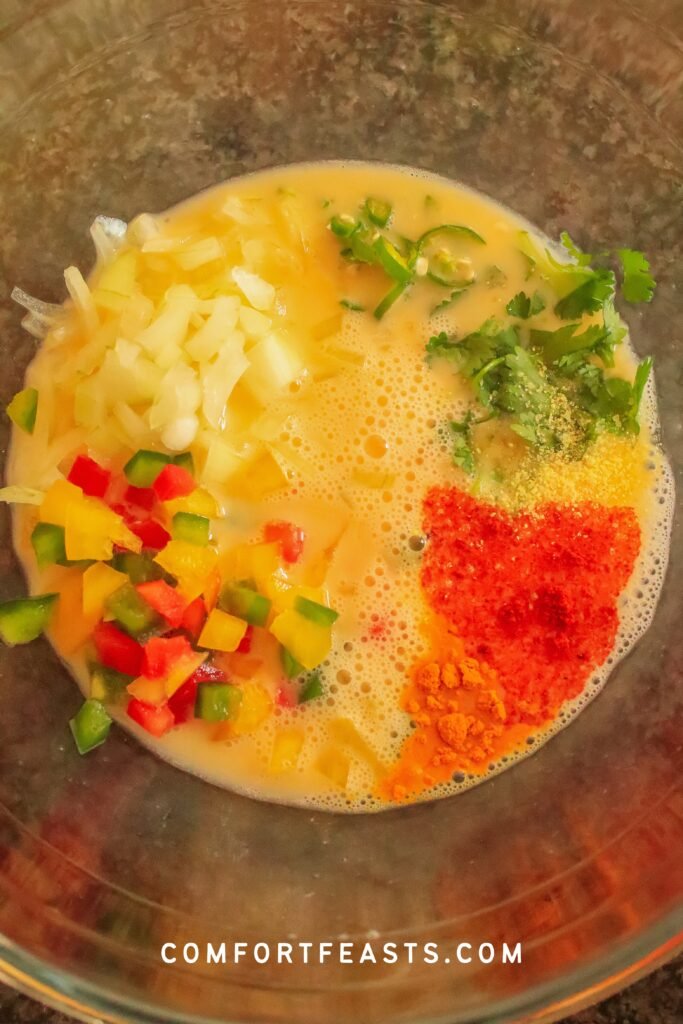 Bowl of whisked eggs mixed with chopped onion, green chili, bell peppers, spices and coriander