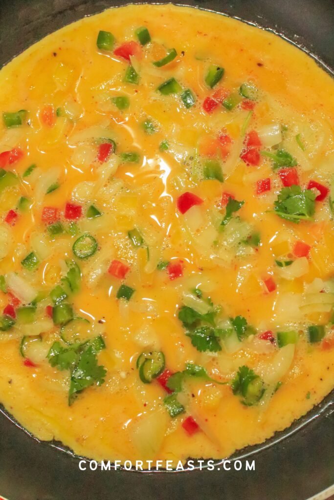 Masala omelette cooking in a buttered pan