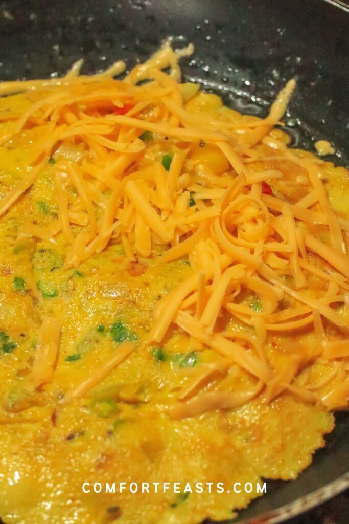 Masala omelette cooking golden in a buttered pan with cheese